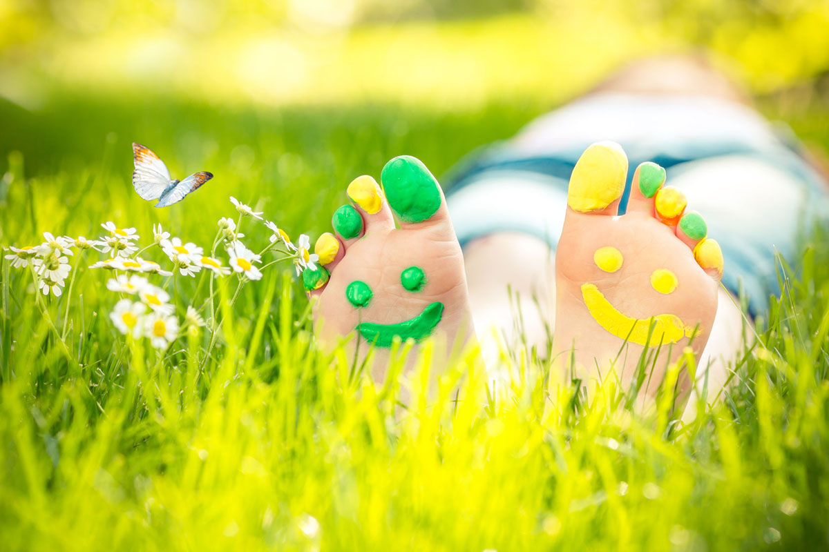 Child lying on green grass with smiley faces painted on feet.