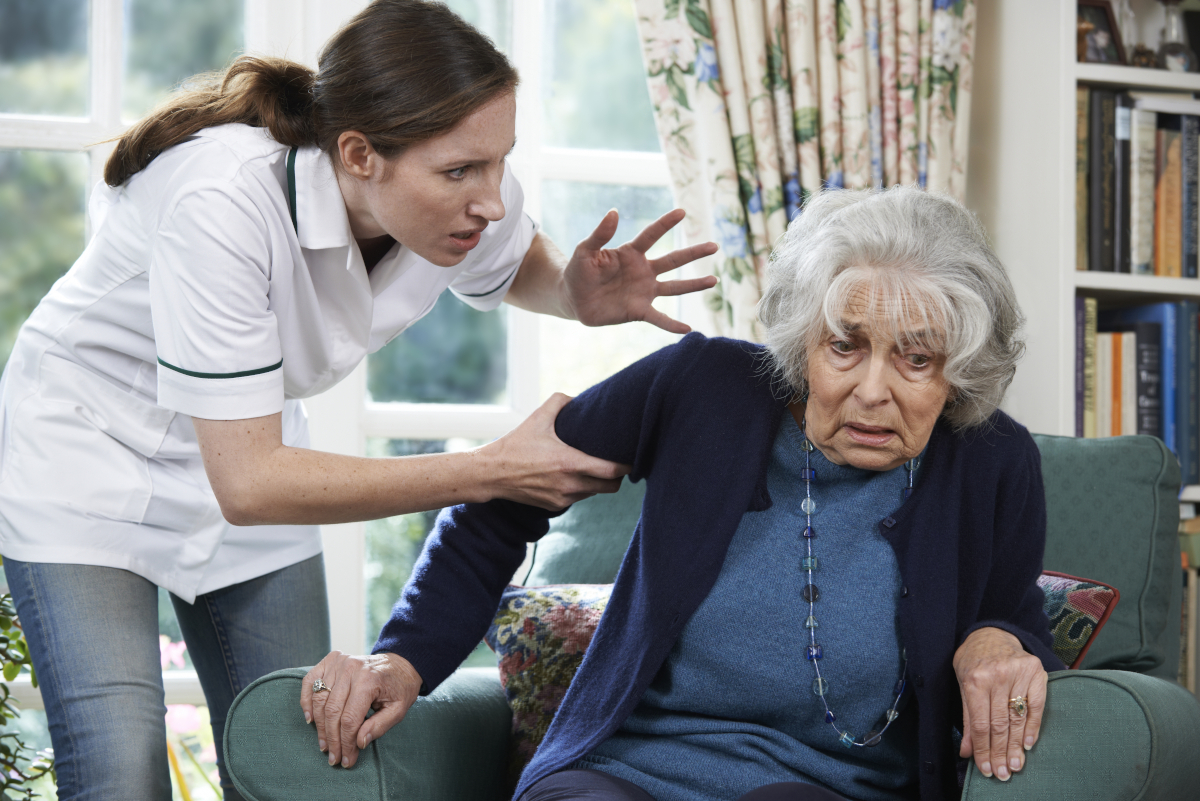 An angry nurse aggresively grabing a scared senior woman.