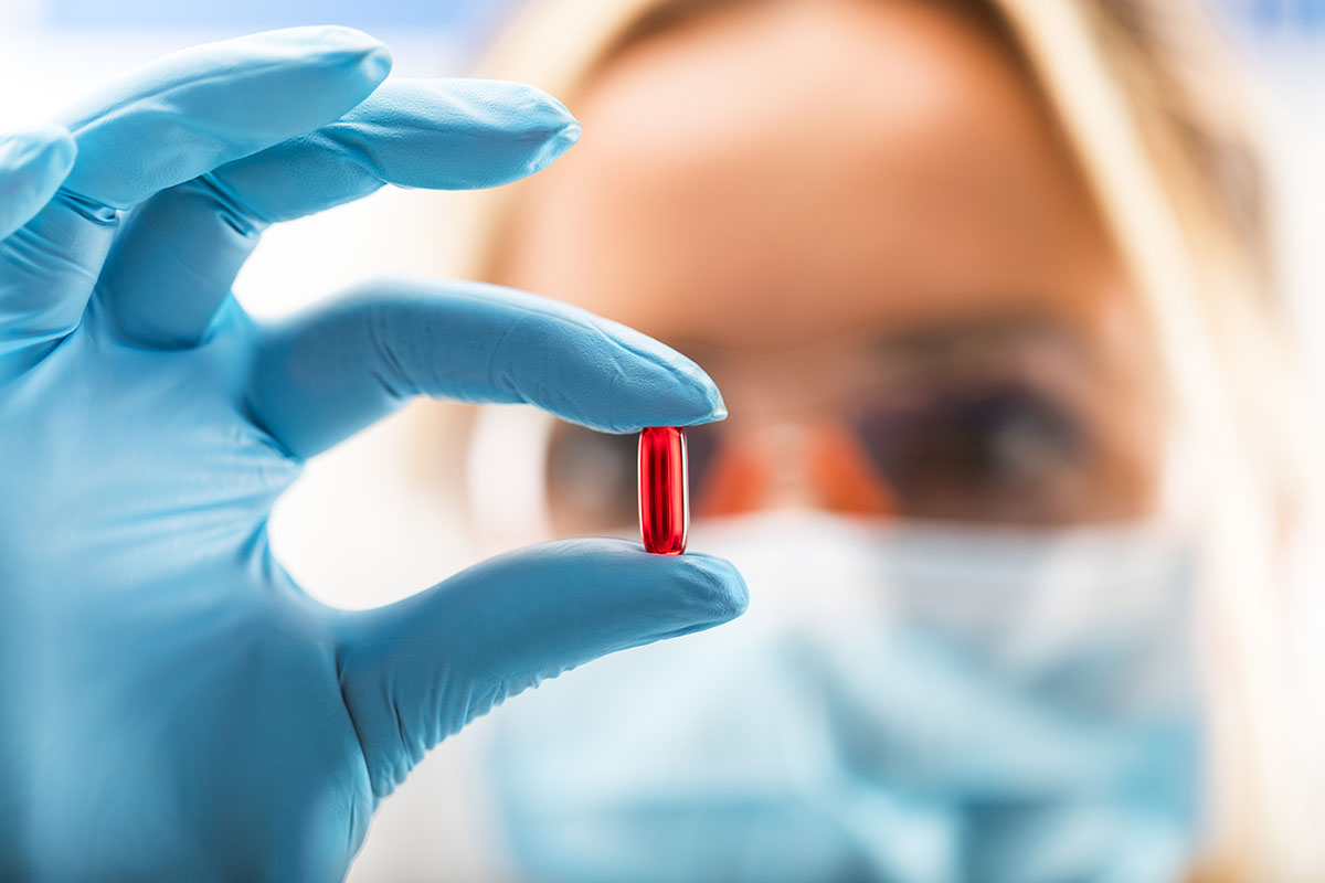 Medical lab technician holding red pill up to camera.